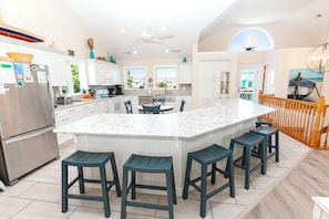 A spacious kitchen with a large island, bar stools, and a view of the outside. - Oceanside, Hot Tub, Pool Table, Community Pool, CP2, The Green Wave (Corolla)