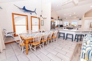 A spacious kitchen with white cabinets, a central island, and a dining area with a wooden table and chairs. - Oceanside, Hot Tub, Pool Table, Community Pool, CP2, The Green Wave (Corolla)