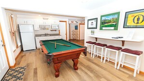 Une table de billard dans une pièce qui comprend un coin cuisine, des tabourets de bar et des tableaux encadrés accrochés au mur.