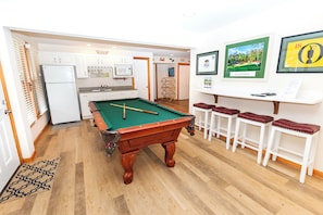 A pool table in a room with a kitchen area, bar stools, and framed pictures on the wall. - Oceanside, Hot Tub, Pool Table, Community Pool, CP2, The Green Wave (Corolla)