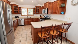 A kitchen with wooden cabinets, a stainless steel refrigerator, a microwave, and a large island with bar stools. - Oceanside, Comm Amenities, Priv Pool, Close to Beach, Rec Rm, 219, Turtle Cove (Corolla)