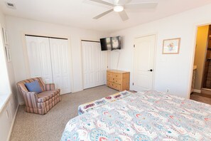 Ein Schlafzimmer mit Bett, Sessel, Kommode, Fernseher und einer Tür.