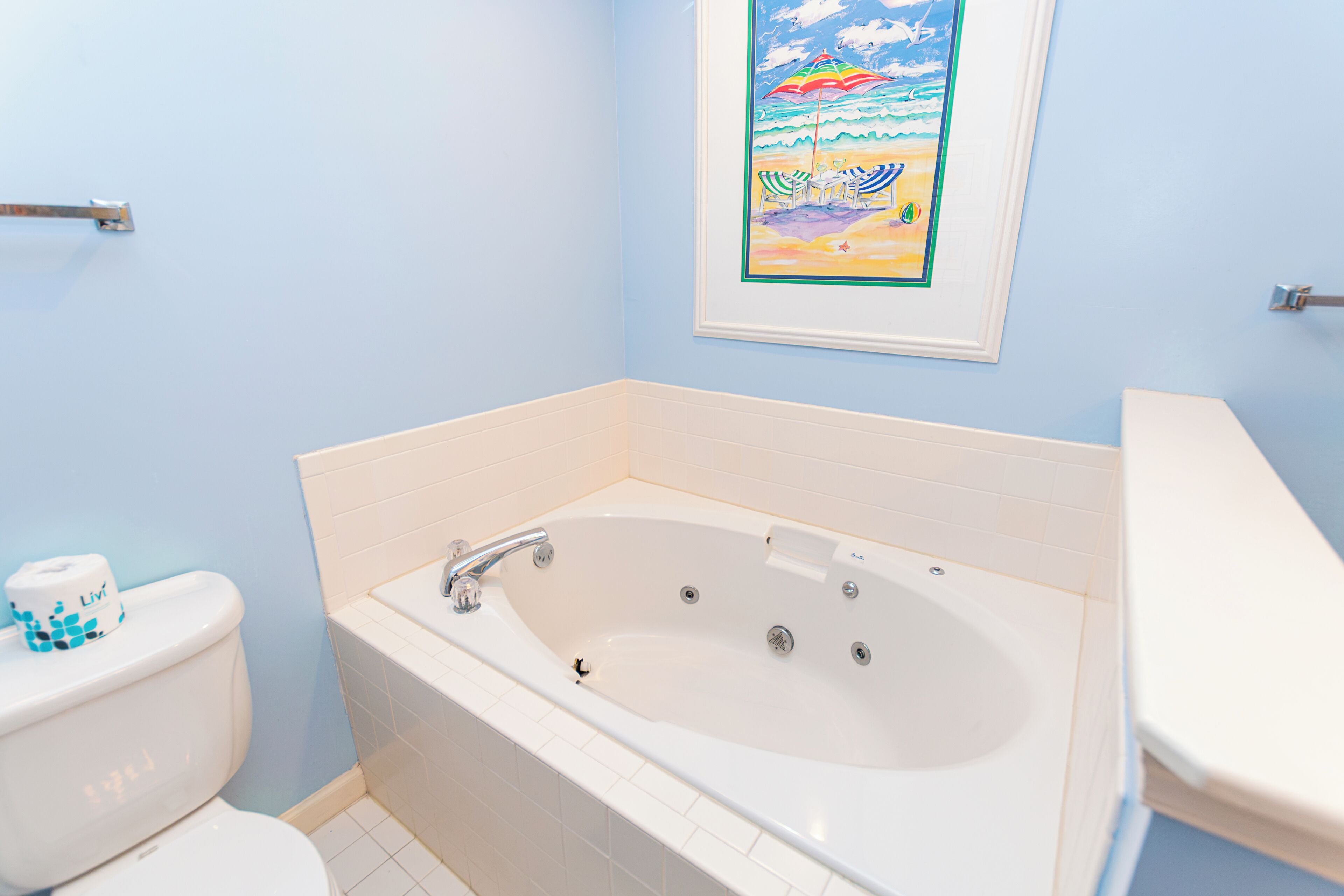 A bathroom with a bathtub, toilet, and a framed picture on the wall.