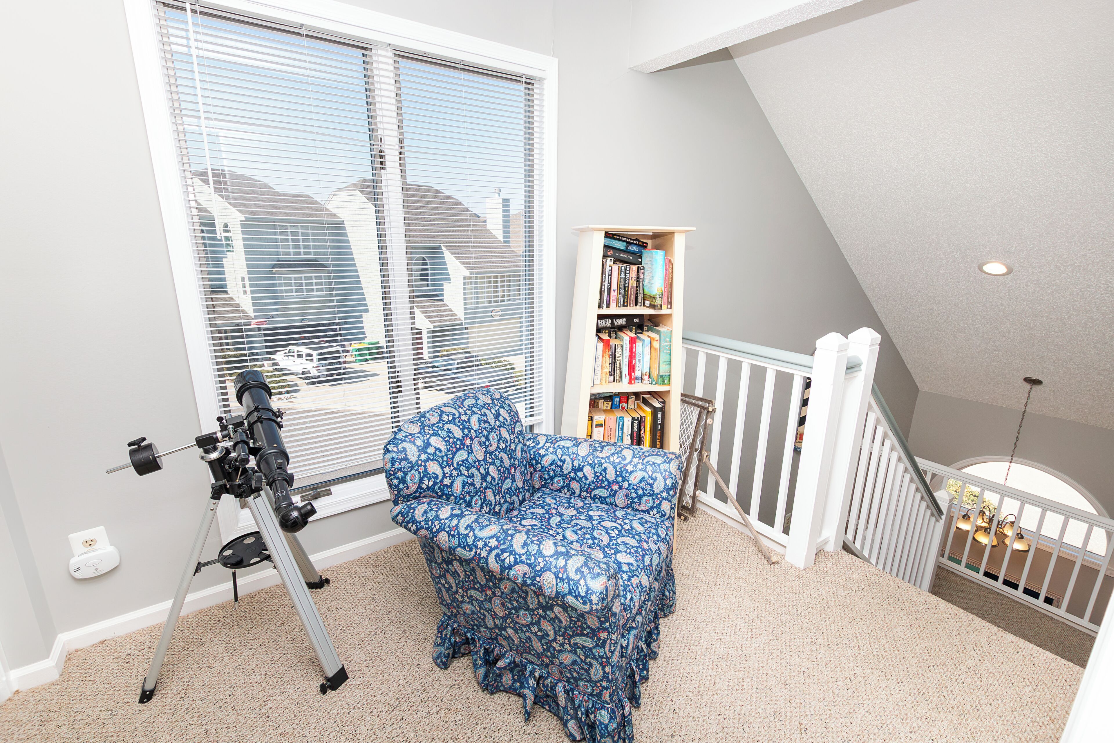 Een kamer met een telescoop, een gestreept sofa, een boekenplank en een ledikant.