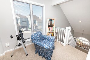 A room with a telescope, a patterned sofa, a bookshelf, and a crib.