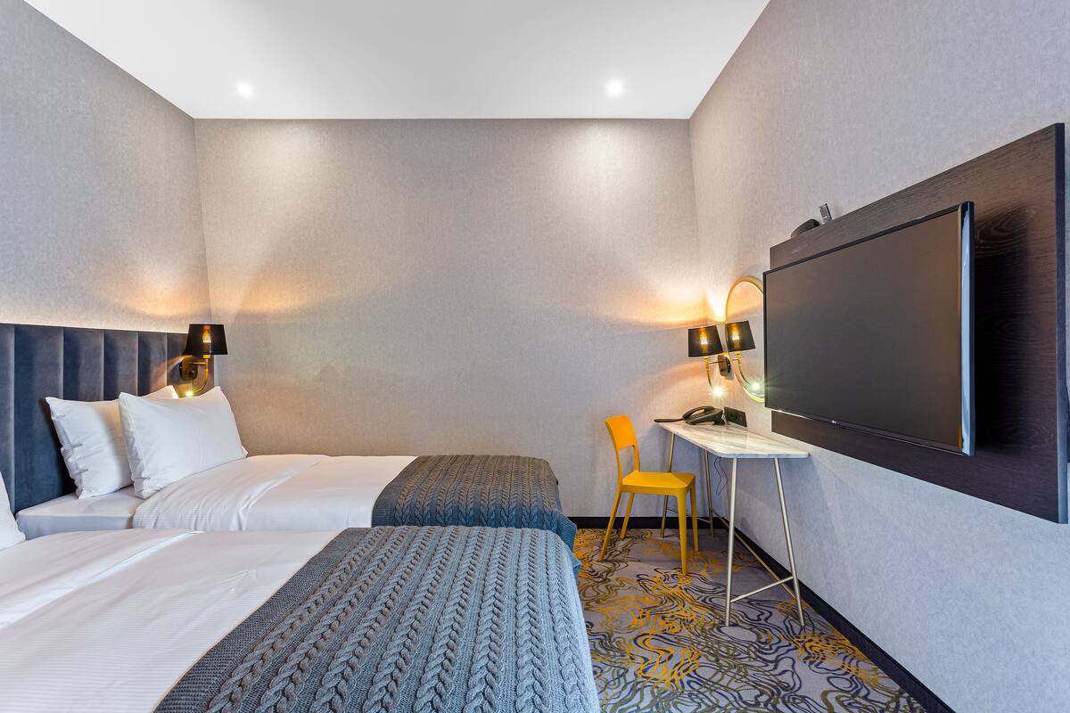 A hotel room with two beds, a desk, a chair, and a large TV.