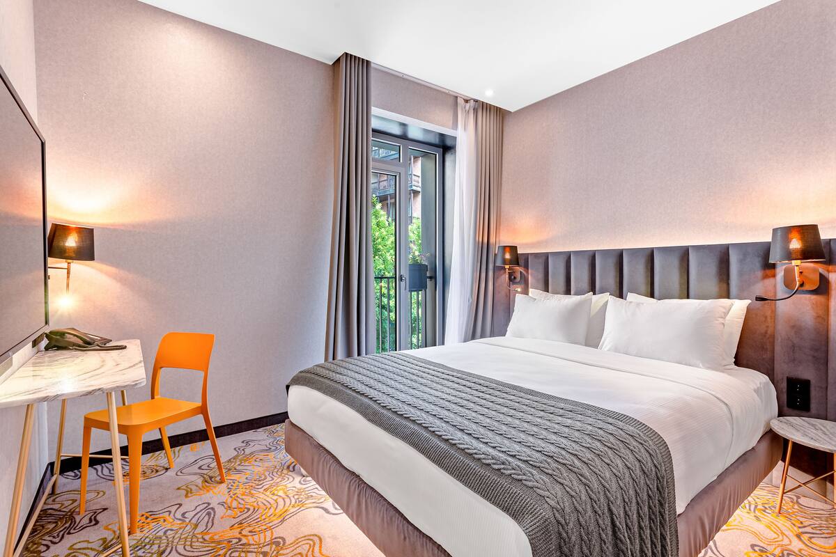 A modern hotel room with a large bed, a desk, and an orange chair.
