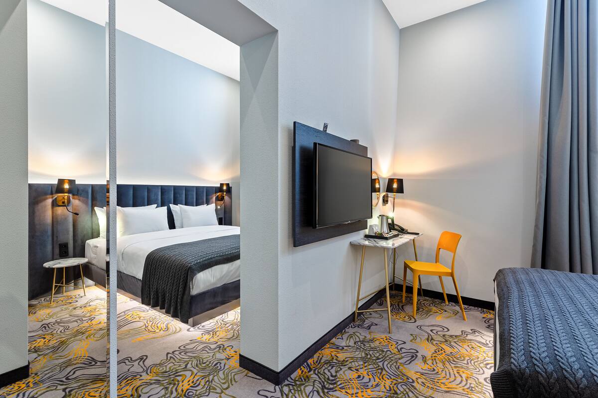 A hotel room with a bed, a TV, a desk with a chair, and a mirror.