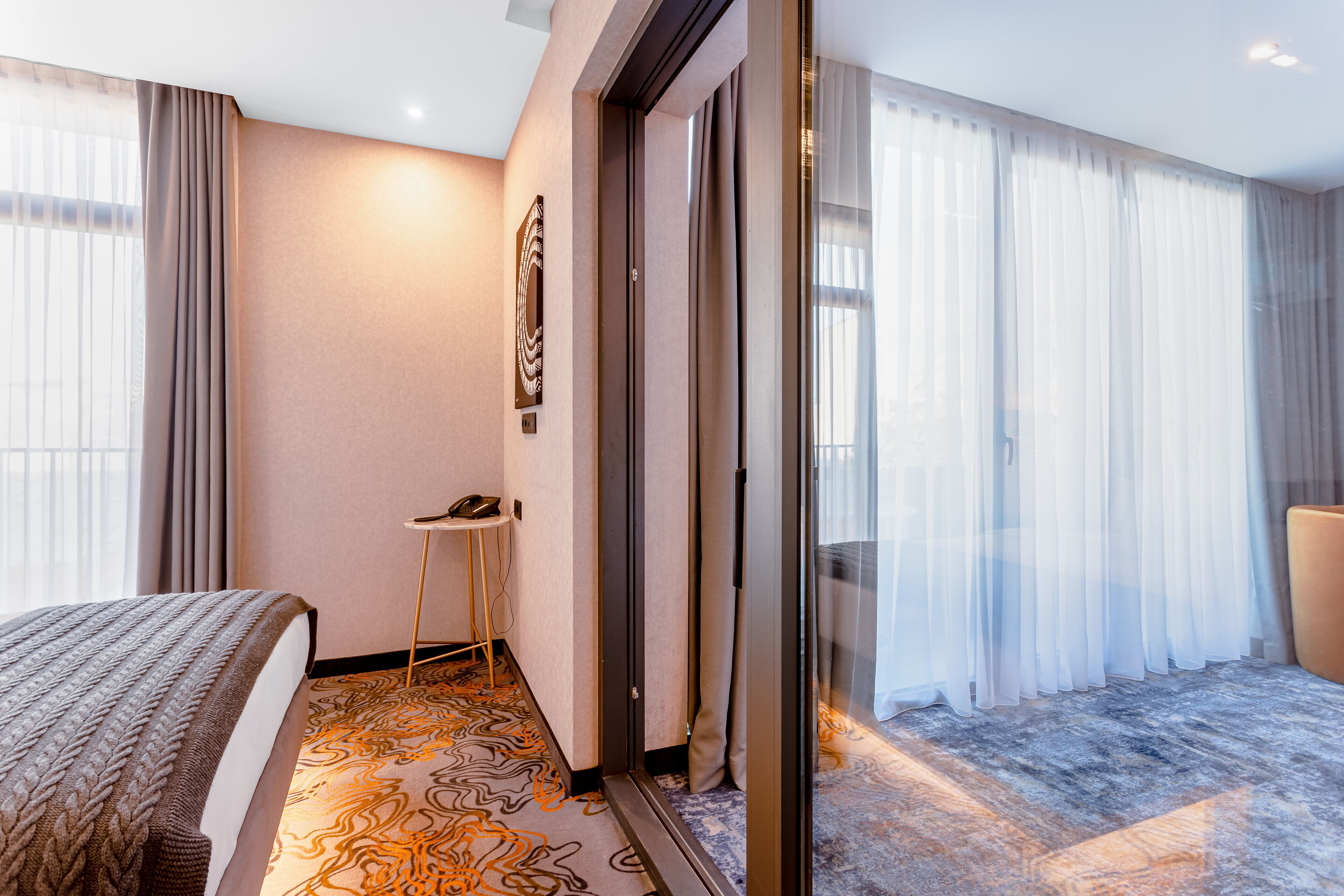 Una camera d'albergo con un letto, una scrivania, un telefono e un'ampia finestra con tende.