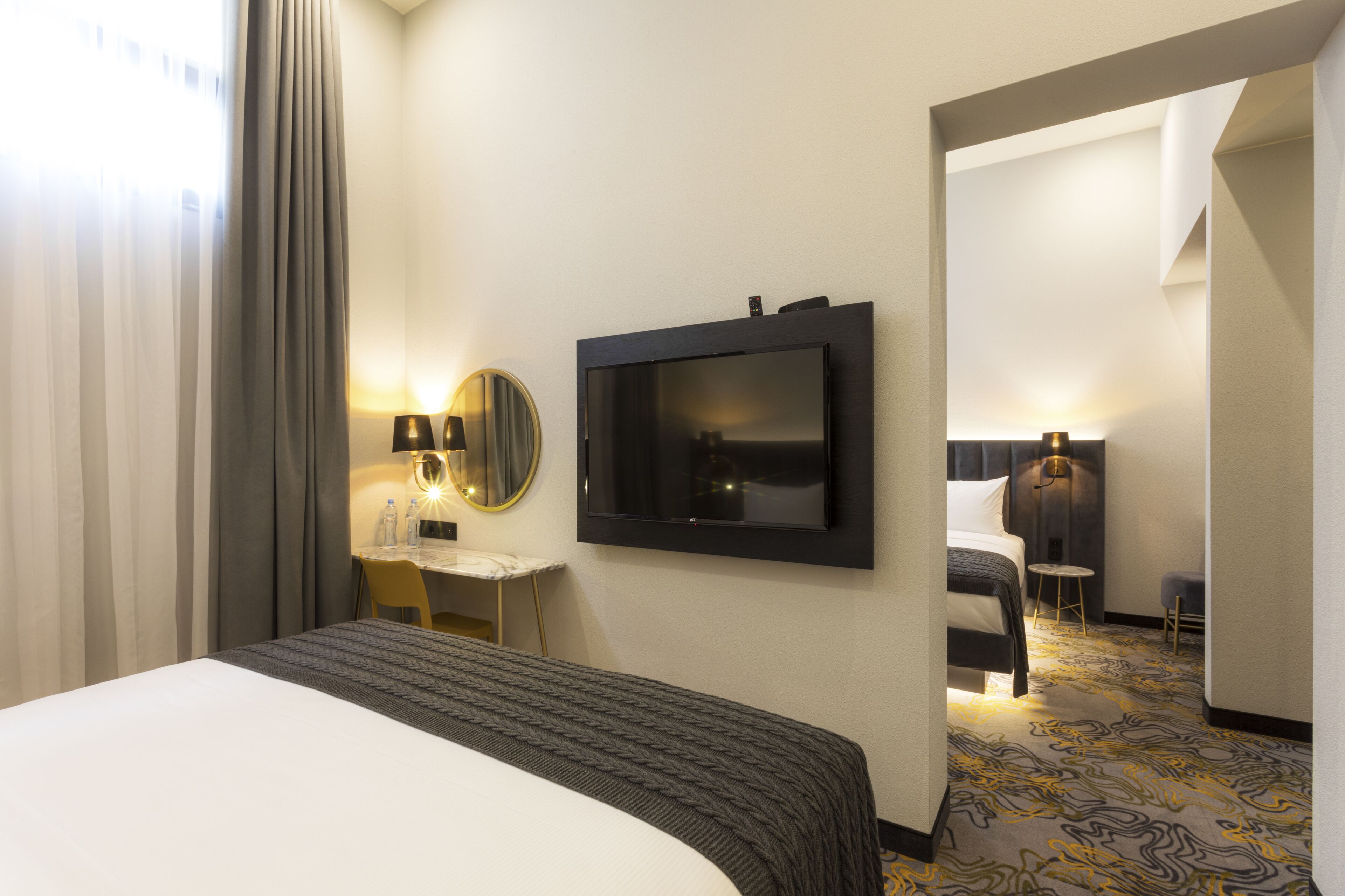 A hotel room with a large bed, a desk with a chair, a television mounted on the wall, and a bathroom visible through an open door.