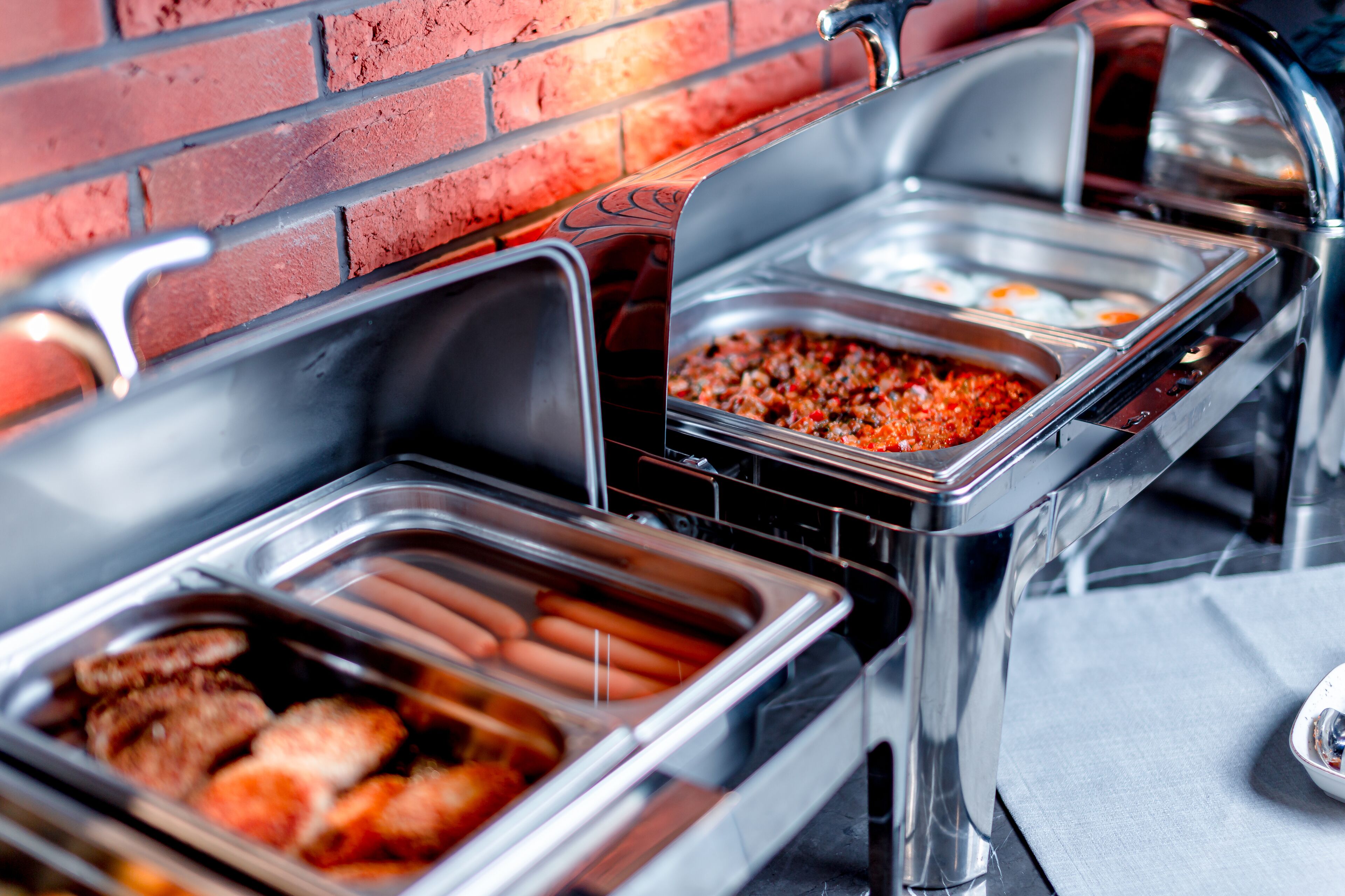 En buffet med forskellige spisemuligheder, herunder hotdogs, kylling og en chili ret.
