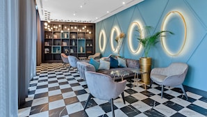 Een moderne lobby met zwart-wit geruit tapijt, een zithoek met banken en stoelen, en een decoratieve wand met verlichte ronde motieven.
