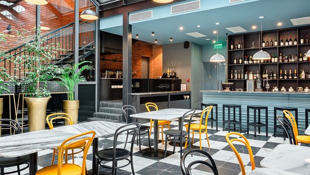 Een restaurant met een schachonzool, zwarte en gele stoelen, en een bar met flessenrekken.
