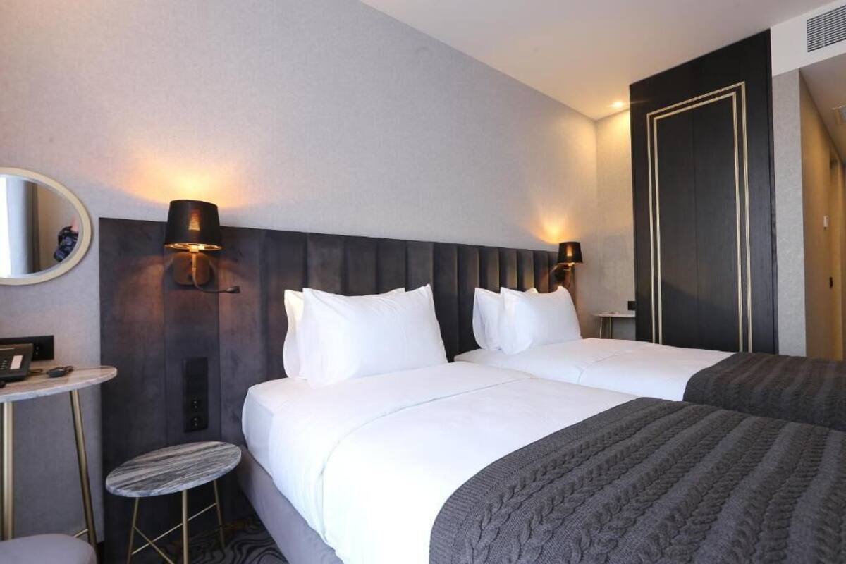 A hotel room with two beds, a round mirror, a small round table, and a wall-mounted lamp.