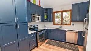 A modern kitchen with blue cabinets, stainless steel appliances, and a wooden floor. - Soundfront, Private Pool, Hot Tub, Sound Views, Community Amenities, 345, Carolina Sunset (Corolla)