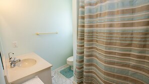 A bathroom with a sink, toilet, and striped shower curtain. - OCEANFRONT, 4-wheel drive area, Wild Horses, Ocean Views! 4x1662, Dolphin Watch (Corolla)