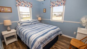 A bedroom with a bed, two bedside tables, a chair, a fan, and two windows with curtains. - OCEANFRONT, 4-wheel drive area, Wild Horses, Ocean Views! 4x1662, Dolphin Watch (Corolla)