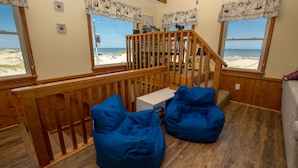 A room with a wooden staircase, a view of the beach, and two blue bean bags. - OCEANFRONT, 4-wheel drive area, Wild Horses, Ocean Views! 4x1662, Dolphin Watch (Corolla)