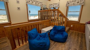 Une pièce avec un escalier en bois, une vue sur la plage et deux fauteuils en forme de sac bleu.