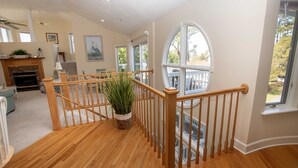 A spacious living area with a wooden staircase, a fireplace, and a large window offering a view of the outdoors. - Soundside, Community Amenities, Sun Decks, 327, Footprints by the Sound (Corolla)