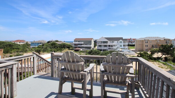 A wooden deck with two Adirondack chairs overlooking a beach and buildings. - Oceanside, Private Pool, Sun Decks, 660 ft to beach access! -WW951, Momma's Happy, Daddys Broke (Corolla)