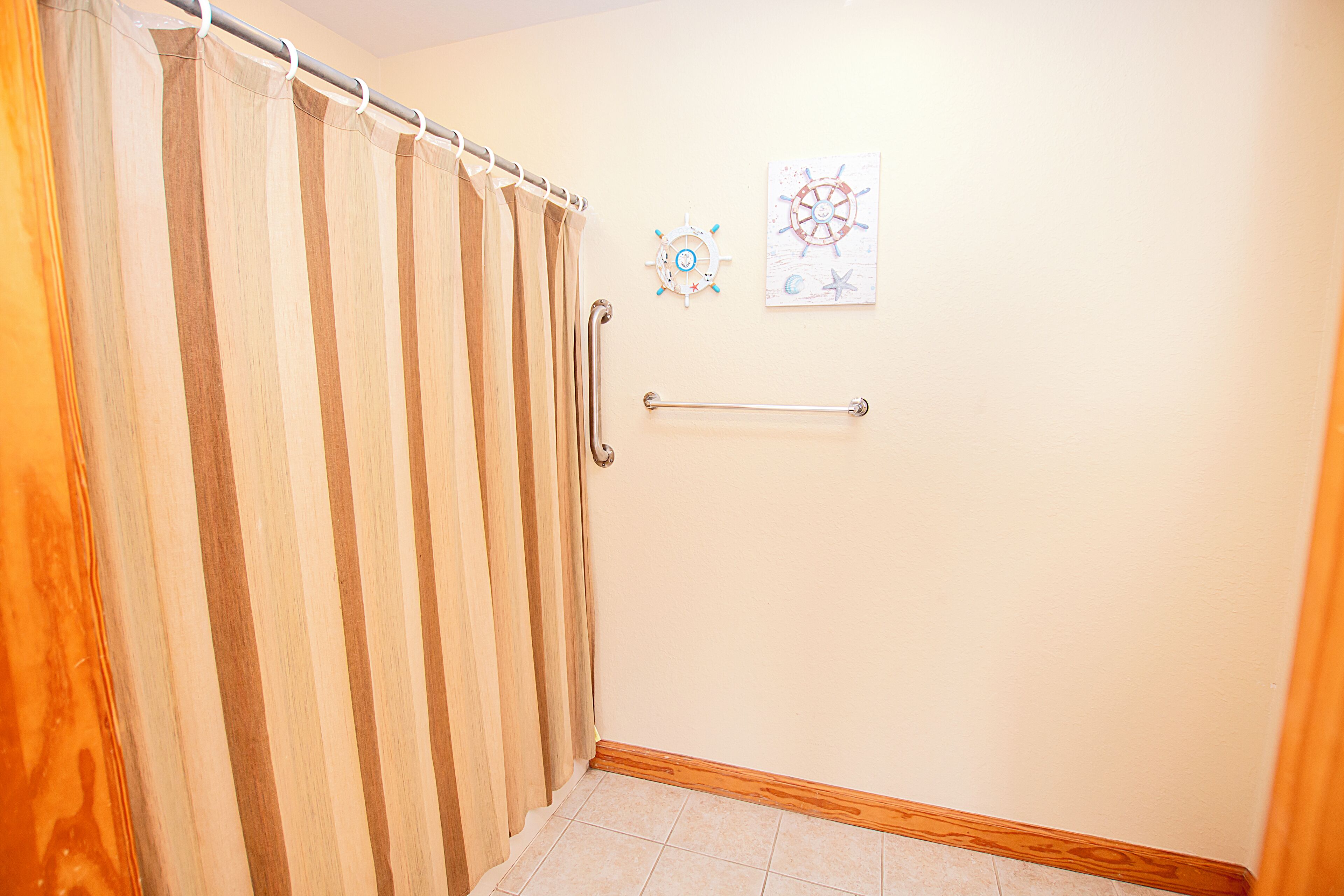 A bathroom with a shower curtain, a handrail, and nautical-themed wall art.