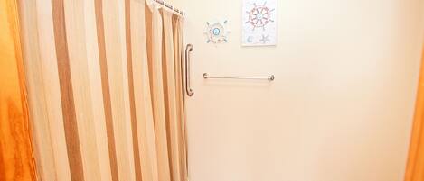 A bathroom with a shower curtain, a handrail, and nautical-themed wall art.