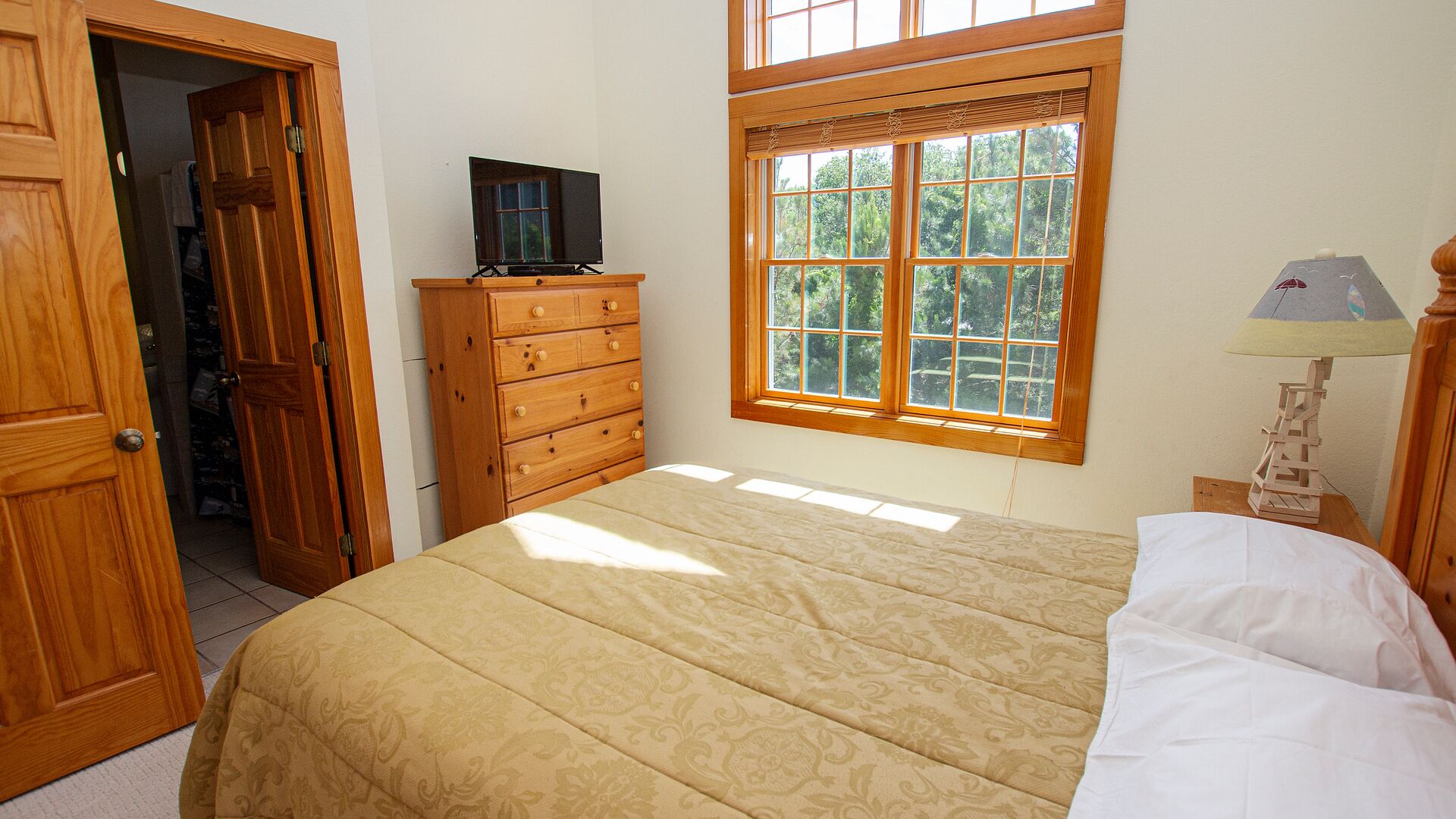 Une chambre à coucher avec un lit, une commode en bois, une télévision, une fenêtre et une lampe.