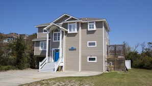 A multi-story residential building with a central staircase, a blue front door, and a sign indicating 'Island So Remote'. - Oceanside, Priv Pool, Hot Tub, OS Shuffleboard, Rec Rm, WW1039, Island So Remote (Corolla)