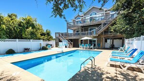 A swimming pool with lounge chairs, a wooden deck, and a multi-story building with balconies. - Oceanside, Priv Pool, Hot Tub, OS Shuffleboard, Rec Rm, WW1039, Island So Remote (Corolla)
