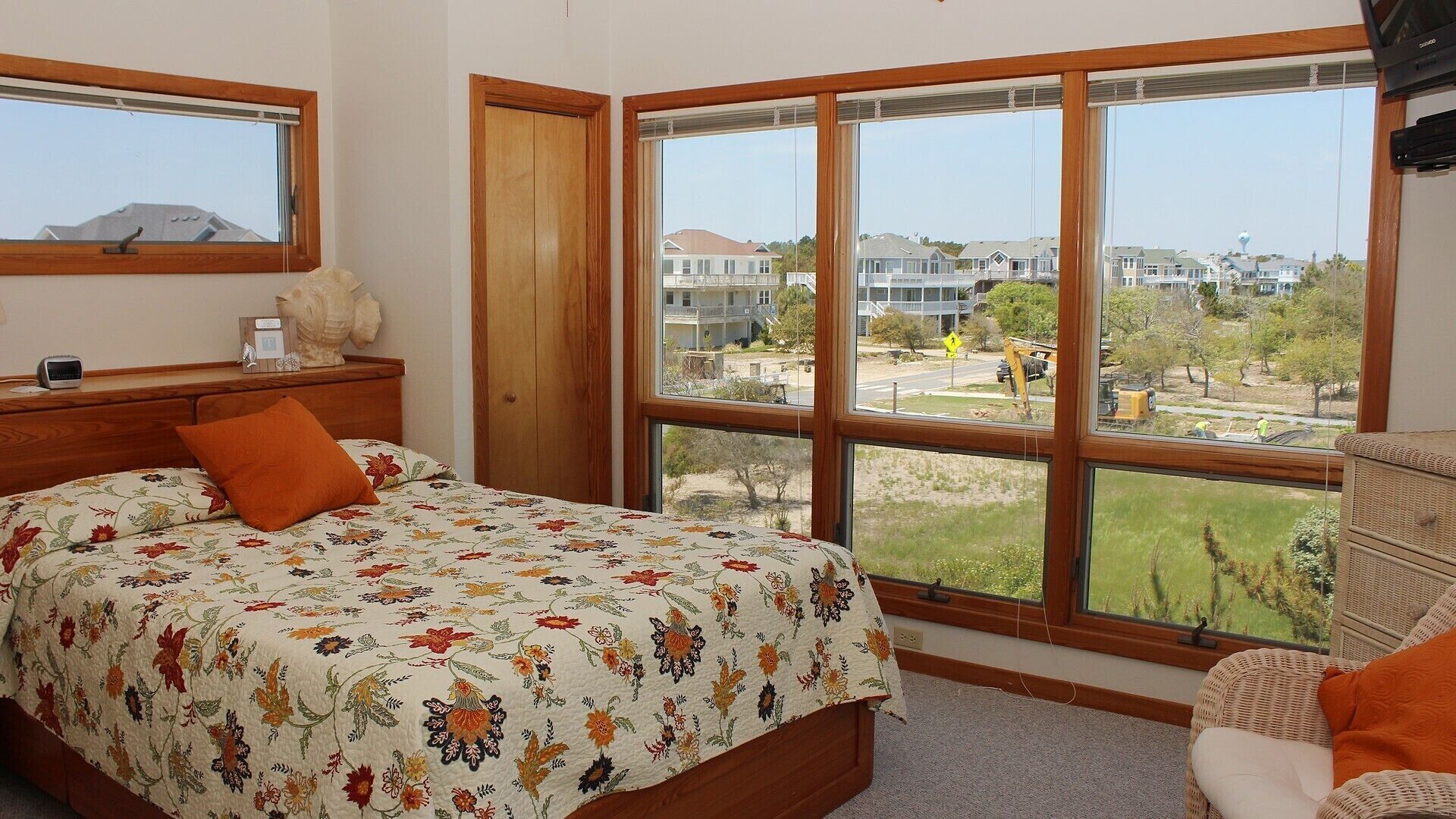 A bedroom with a large window, a bed with floral bedding, a nightstand, and a chair.