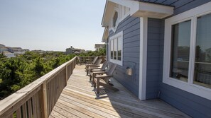 Une terrasse en bois avec des chaises, une rambarde et une maison dotée de grandes fenêtres.
