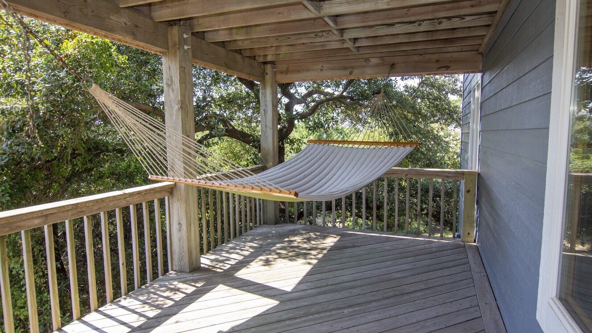 A wooden deck with a hammock, wooden railings, and a view of trees.