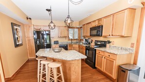 A kitchen with wooden cabinets, granite countertops, a stainless steel refrigerator, a microwave, and a sink. - Oceanside, Community Amenities, Hot Tub, Sun Decks, 117, Sound Waves (Corolla)