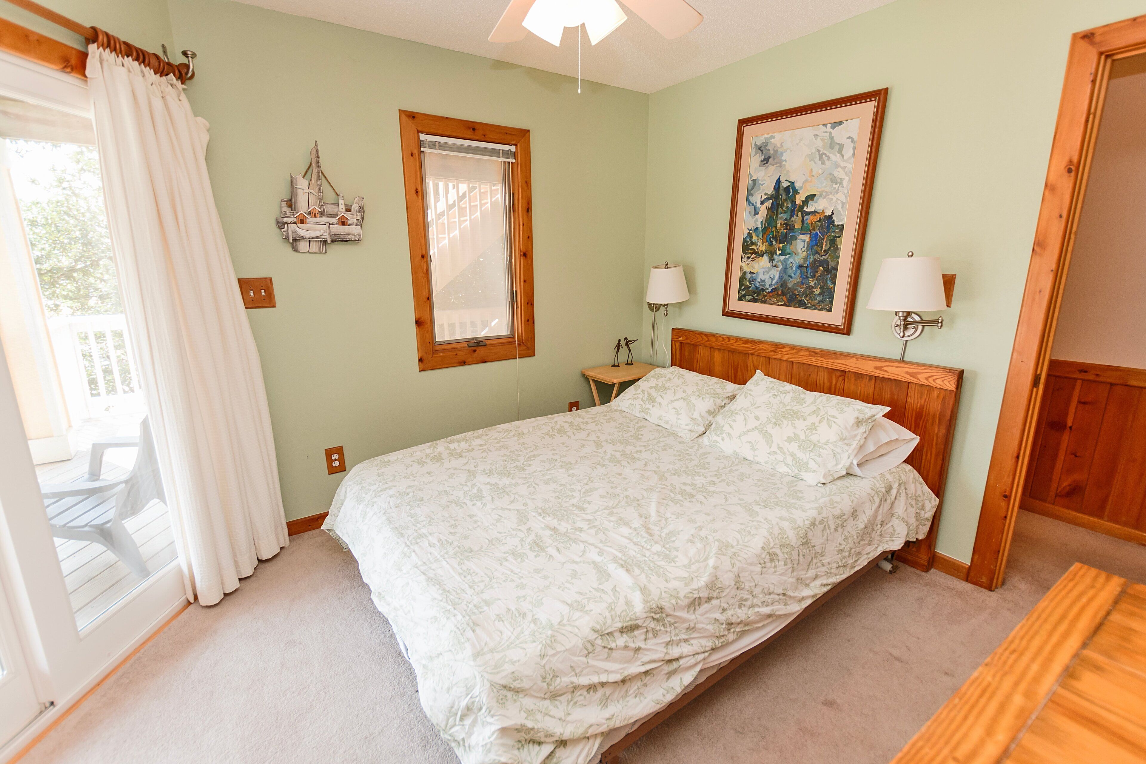 A bedroom with a bed, a window with curtains, a bedside table with a lamp, and a painting on the wall.