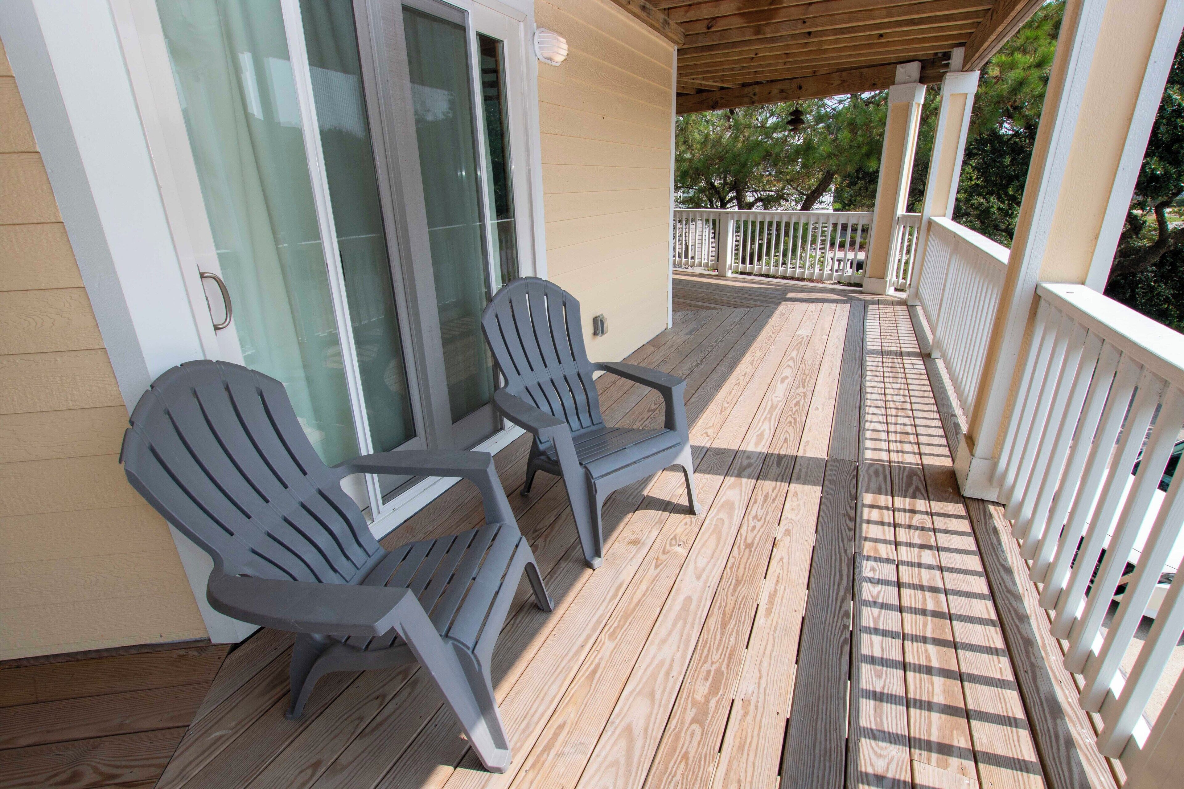 Une terrasse en bois avec deux fauteuils Adirondack, une porte vitrée et une rambarde blanche.