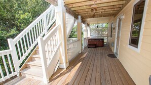 A wooden deck with a white railing, a covered area with a ceiling, and a view of a house in the background. - Oceanside, Community Amenities, Hot Tub, Sun Decks, 117, Sound Waves (Corolla)