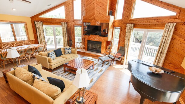 A spacious living room with a fireplace, wooden furniture, and large windows. - Oceanside, Community Amenities, Hot Tub, Sun Decks, 117, Sound Waves (Corolla)
