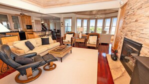 A spacious living room with a large sofa, a rocking chair, and a fireplace. There is a kitchen in the background with wooden cabinets and a dining area with chairs. - Oceanside, Screened Porch, 100 ft to Beach Access, SA180, Siren Song (Duck)