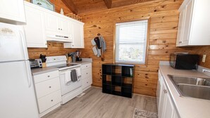 Pieni, käytännöllinen keittiö, jossa on valkoiset kaapit, liesi ja pesuallas.