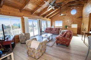 Un salon spacieux doté de plafonds en bois, d’un ventilateur de plafond et de grandes fenêtres offrant une vue sur l’extérieur.