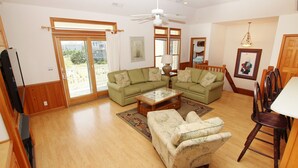 A spacious living room with a large sectional sofa, a coffee table, and a dining area with a table and chairs. - Oceanside, 7 BRs, ELEVATOR, Private Pool, Hot Tub, OH3, Aurora (Corolla)
