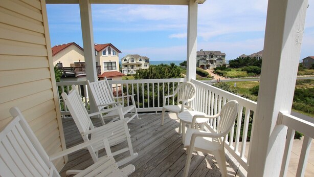 A wooden deck with white chairs and a railing, overlooking a residential area with houses and a clear sky. - Oceanside, 7 BRs, ELEVATOR, Private Pool, Hot Tub, OH3, Aurora (Corolla)