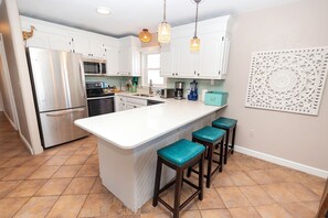 A kitchen with white cabinets, stainless steel appliances, a central island with stools, and a decorative wall piece.