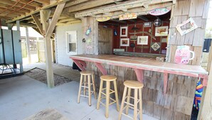 Un área de bar al aire libre con estructura de madera, mostrador, taburetes y diversas decoraciones.