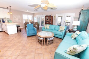 A spacious living area with a dining table, blue sofas, and a kitchen in the background.