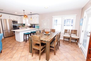 A modern kitchen with white cabinets, a stainless steel refrigerator, and a wooden dining table with chairs.