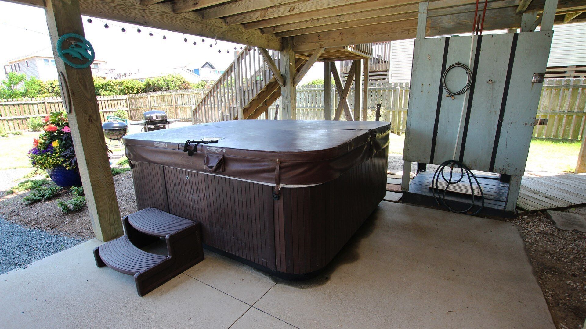 A hot tub under a wooden pergola with a wooden bench and a hose.