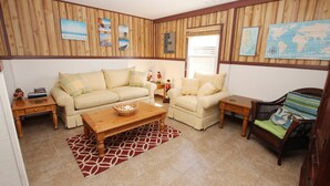 A cozy living room with a beige sofa, a wooden coffee table, and a wicker chair. - Oceanside, 5 BRs, Hot Tub, Rec Room, Close to Shopping, KH221, Shoebies Hangout (Kitty Hawk)