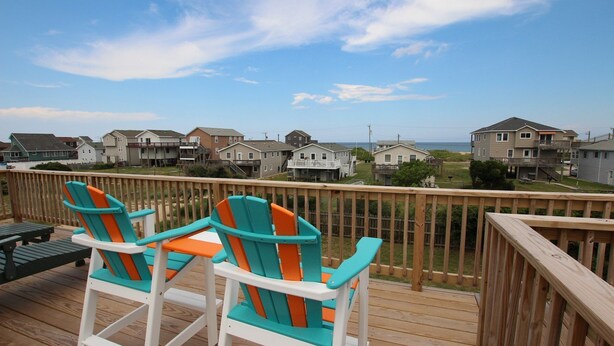 Una terraza de madera con dos sillas Adirondack coloridas orientadas hacia la vista de la playa.